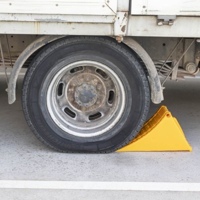 Roda de veículo pesado com pneu preto e calço amarelo de segurança no chão.
