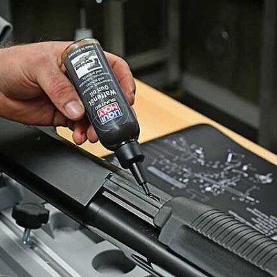 Frasco de óleo lubrificante LIQUI MOLY aplicado em arma preta numa bancada de trabalho