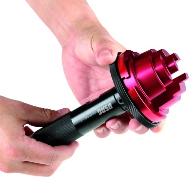 Ferramenta preta com topo vermelho metálico a ser segurada por duas mãos