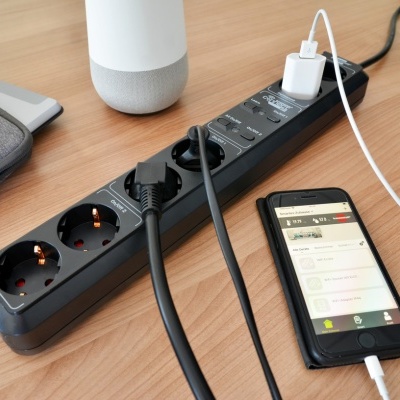 Filtro de linha preto com cabos ligados sobre mesa de madeira clara