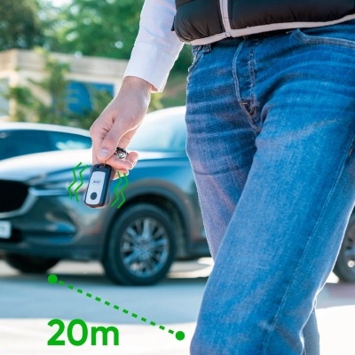 Pessoa com comando remoto para automóvel e carro cinzento ao fundo