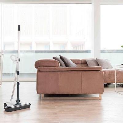 Sofá castanho claro com almofadas e rodo no chão de madeira clara