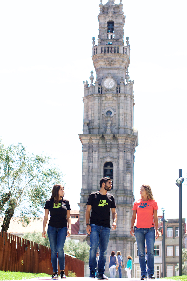 Três pessoas vestindo t-shirts coloridas com fundo da Torre dos Clérigos