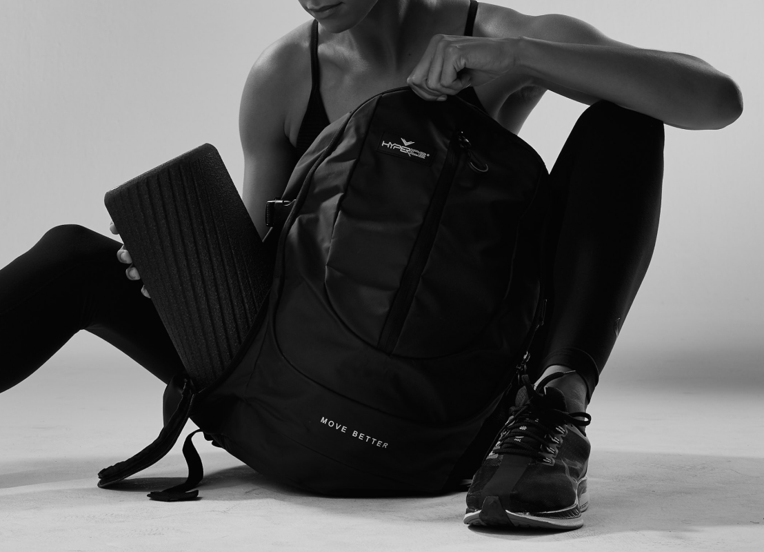 Hyperice Teck Pack Mochila preta com texto MOVE BETTER e tapete de yoga preto em fundo neutro