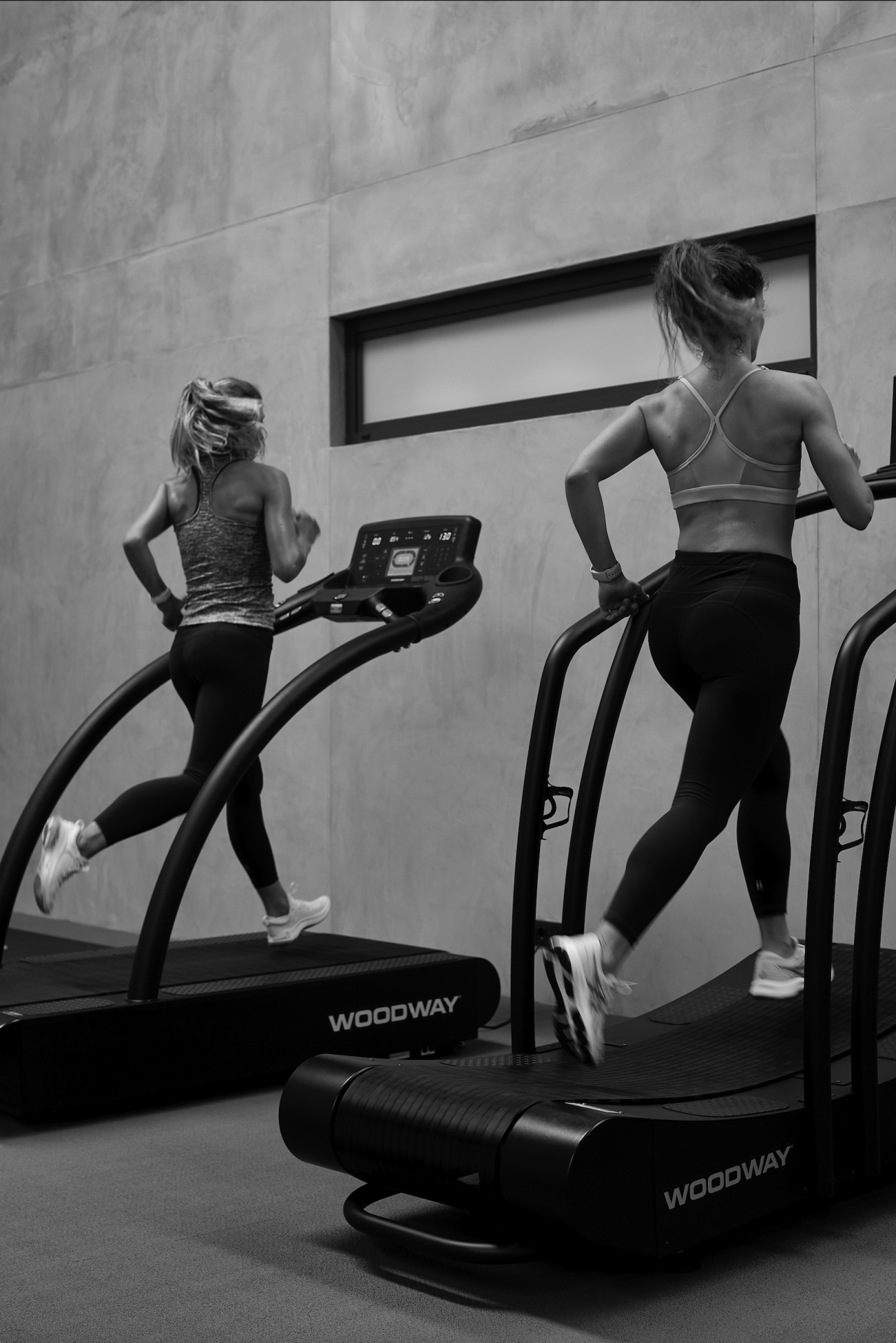 Duas mulheres a correr em passadeiras rolantes negras WOODWAY numa sala interior.