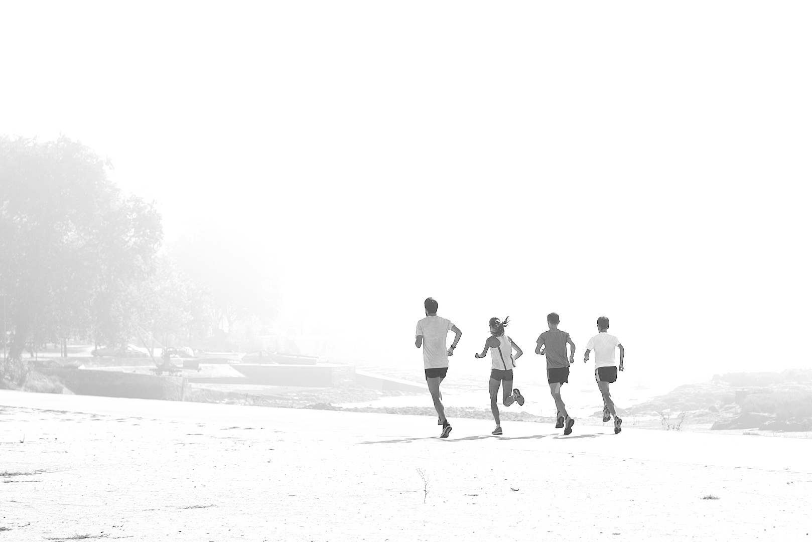 Experiências de treino - Plano básico Quatro pessoas a correr numa praia ampla em preto e branco