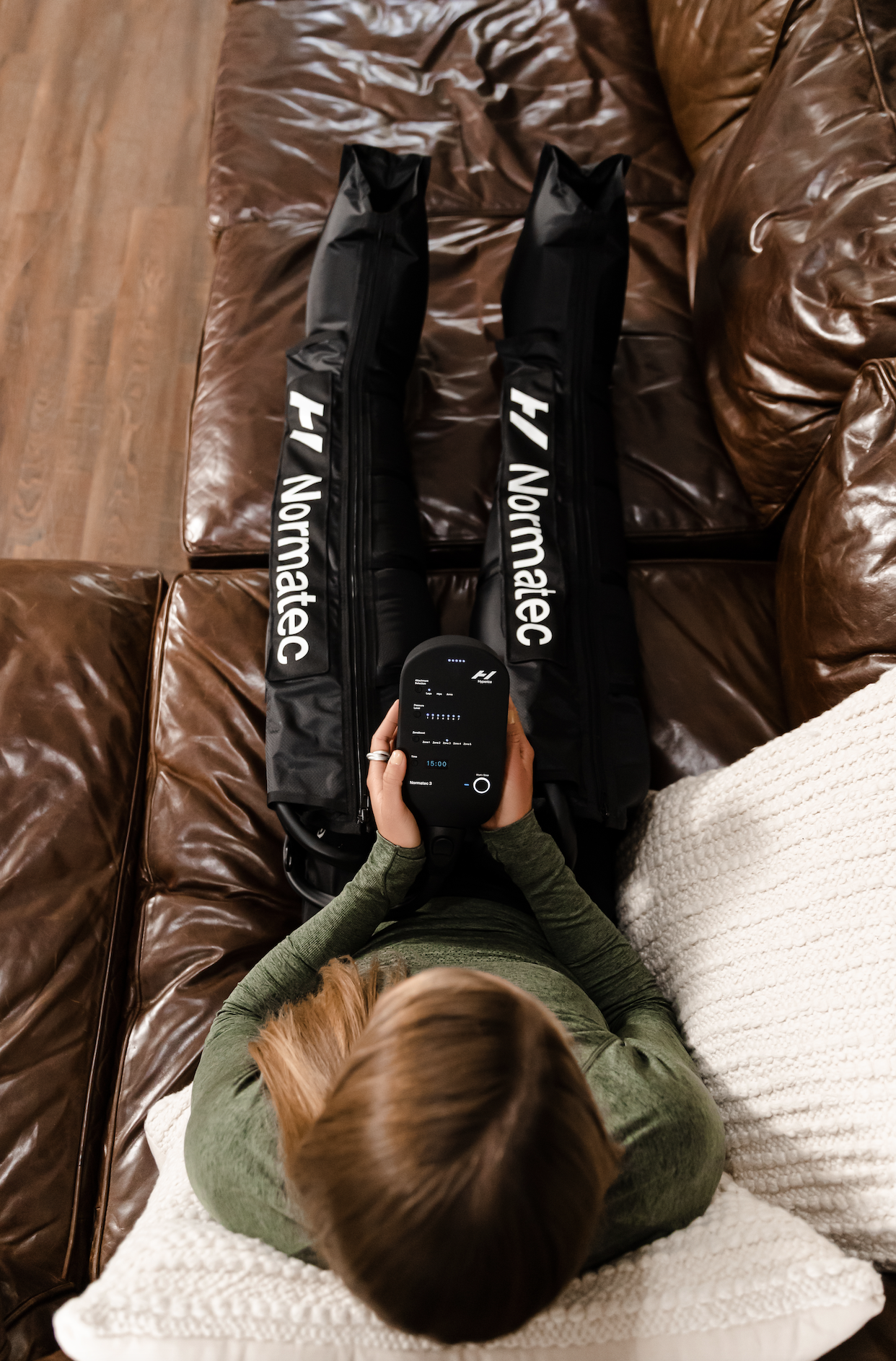 Normatec 3 Pessoa sentada com equipamento de compressão para pernas Normatec preto num sofá de couro castanho