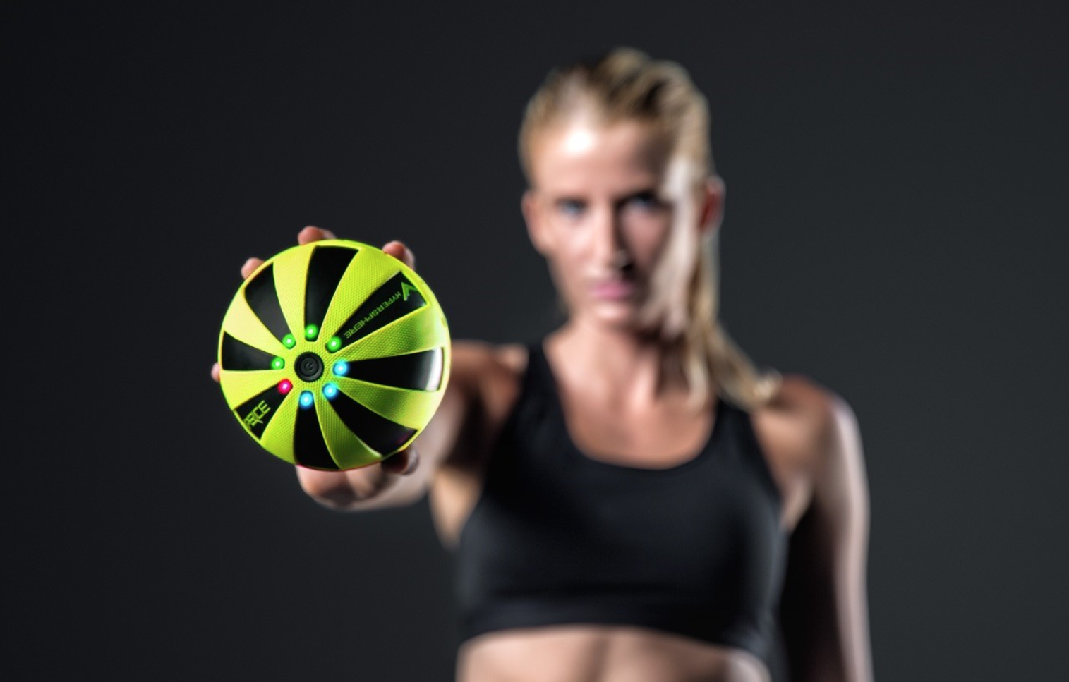 Bola de fitness verde e preta com detalhes azuis segurada por mulher com roupa preta