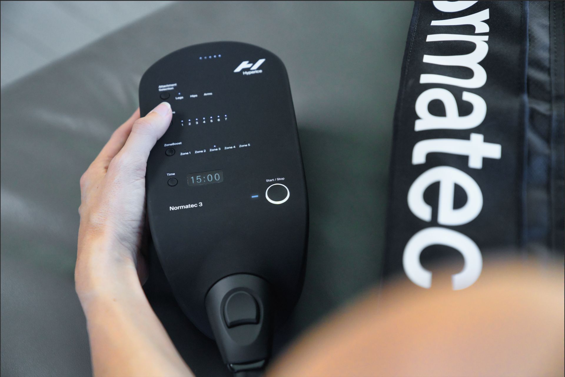 Normatec 3 Dispositivo digital preto com ecrã e botões ao lado de bolsa preta com texto