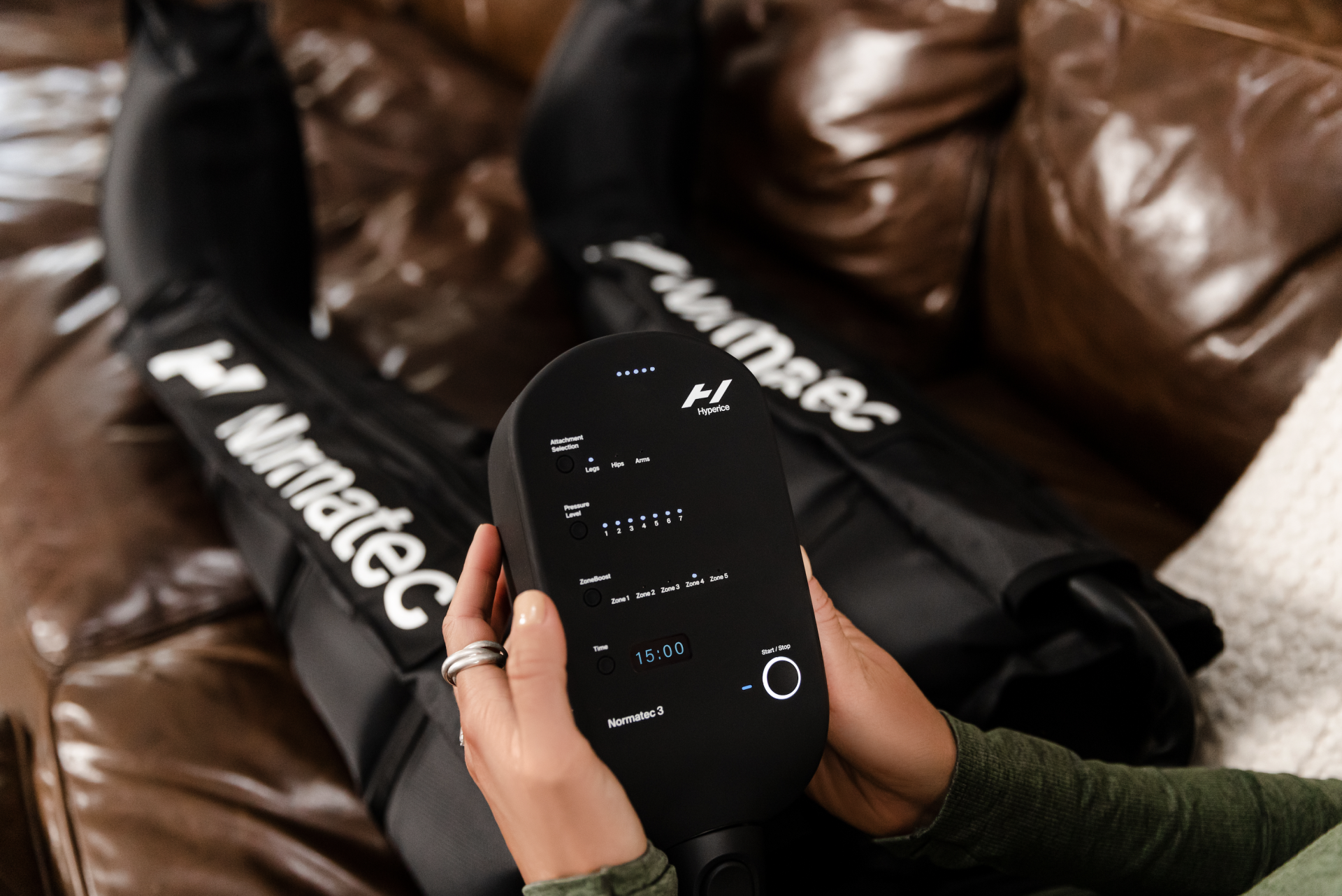 Normatec 3 Aparelho electrónico preto com display digital e mangas pretas com texto Marnatec num sofá castanho.