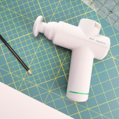 Dispositivo branco de massagem 'Hyperice' sobre superfície verde com lápis e folha branca