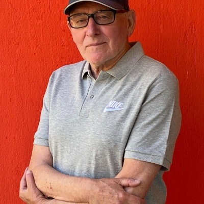 Homem idoso com boné e polo Nike cinzento em fundo laranja