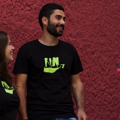 Três pessoas vestem t-shirts com letras e gráficos coloridos frente a parede vermelha.