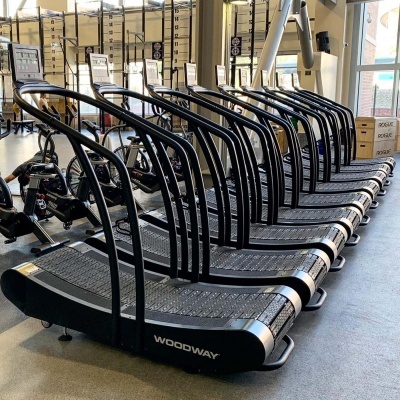 Tapetes de corrida curvos WOODWAY alinhados num ginásio com chão cinzento