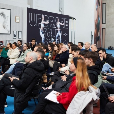 Pessoas sentadas a assistir numa sala com painel preto e texto visível