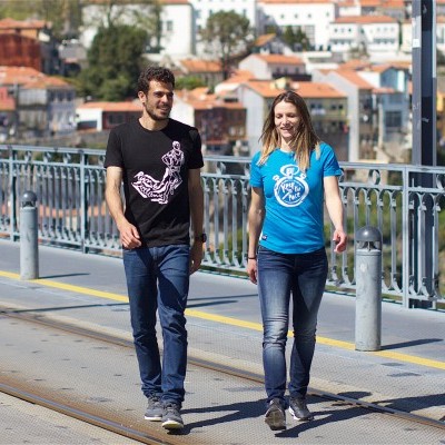 Dois adultos com t-shirts estampadas a caminhar numa ponte urbana com carris de elétrico