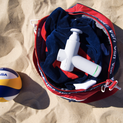 Bola de voleibol Mikasa ao lado de bolsa desportiva vermelha com toalha azul e frasco branco na areia