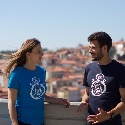 Dois jovens de t-shirts azul e preta com estampa de cronómetro branco com texto em cidade