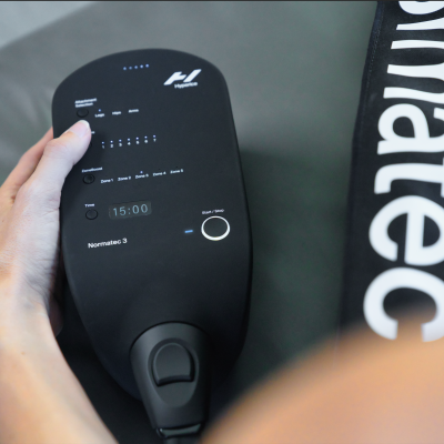 Dispositivo digital preto com ecrã e botões ao lado de bolsa preta com texto