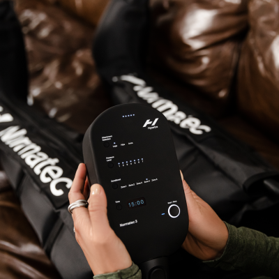 Aparelho electrónico preto com display digital e mangas pretas com texto Marnatec num sofá castanho.