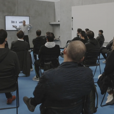 Sala de conferências com apresentação num ecrã e público sentado em cadeiras pretas