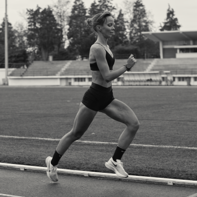 Mulher a correr na pista com roupa desportiva preta e sapatilhas brancas