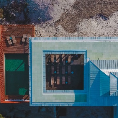 Vista aérea de casa moderna com telhado azul, piscina e área de madeira com cadeiras