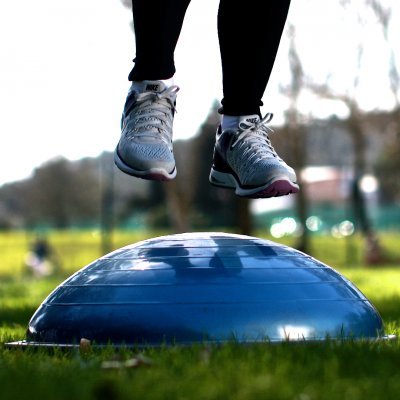Sapatos Nike cinzentos a saltar sobre bola de equilíbrio azul ao ar livre