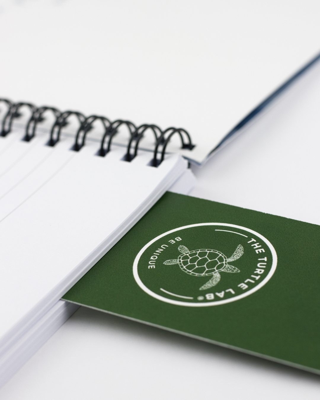 Bloco de notas com espiral preta e cartão verde com logo de tartaruga e texto em branco