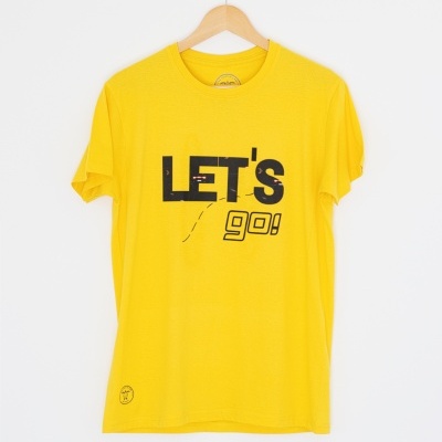 T-shirt amarela com texto LET'S go! em preto e branco, pendurada num cabide de madeira.