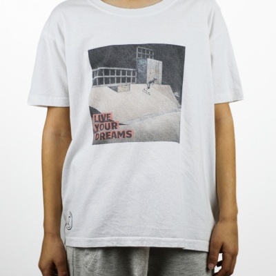 Criança vestindo t-shirt branca com estampa de rampa de skate e texto 