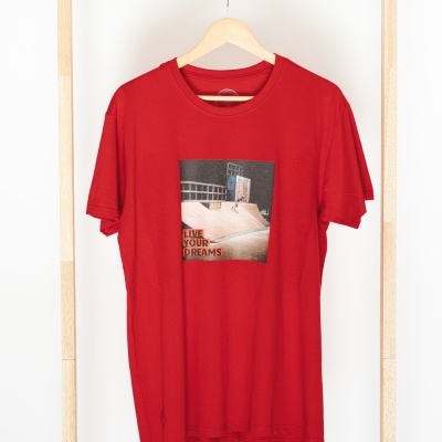 T-shirt vermelha com estampado frontal 'LIVE YOUR DREAMS' pendurada em cabide de madeira