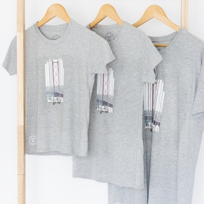 Três t-shirts cinzentas com estampado e texto LSEBA penduradas em cabides de madeira