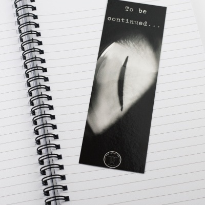 Marcador de páginas preto com imagem de um olho e texto 