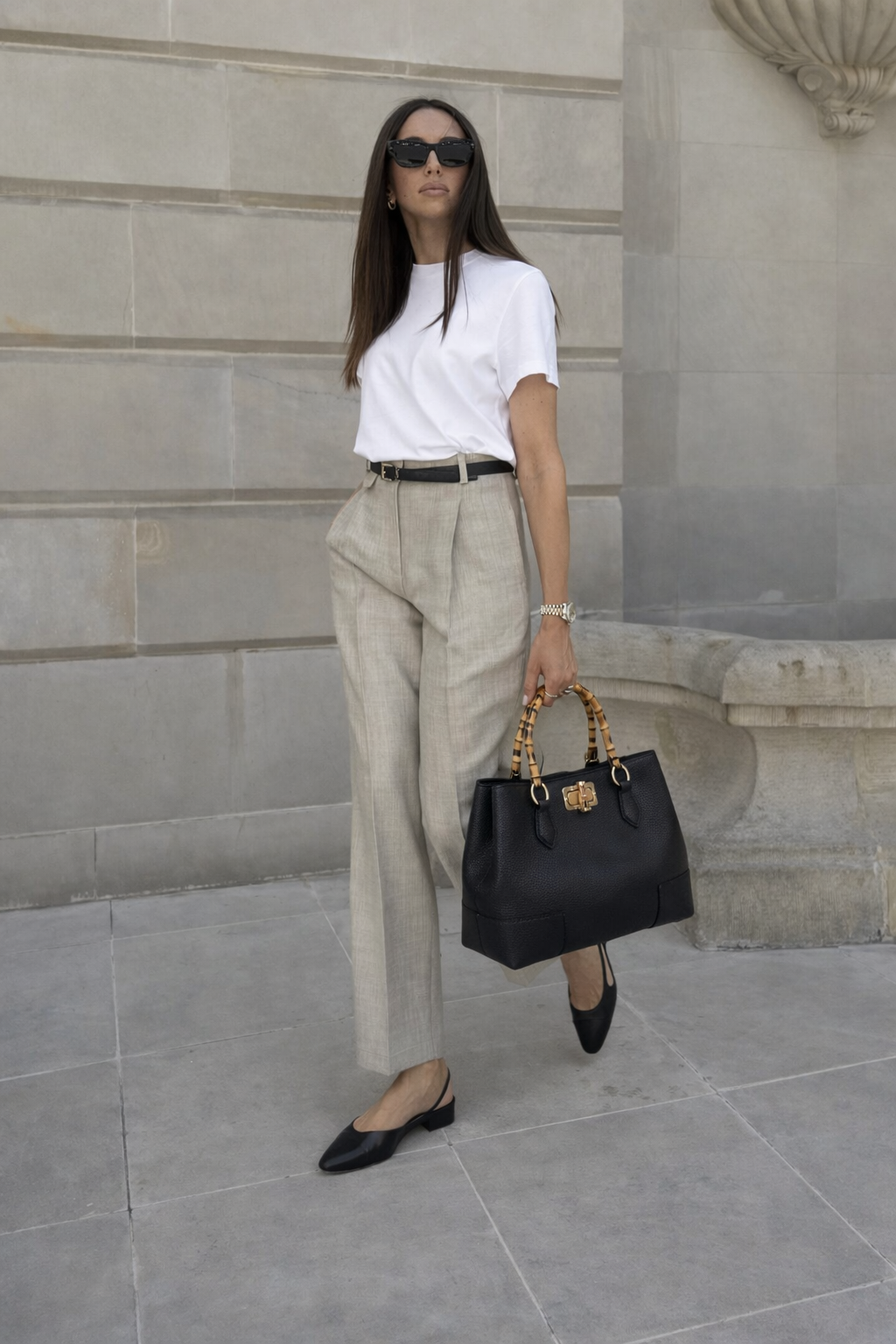 MALA EM PELE ITALIANA AMALFI PRETO | TUSCAN Mulher com t-shirt branca, calças bejes, sapatos pretos e mala preta com pegas de padrão bambu