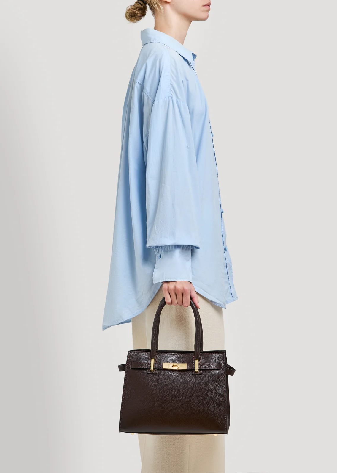 MALA EM PELE ITALIANA PORTOFINO CASTANHO | TUSCAN Mulher com camisa azul clara e mala de mão castanha escura