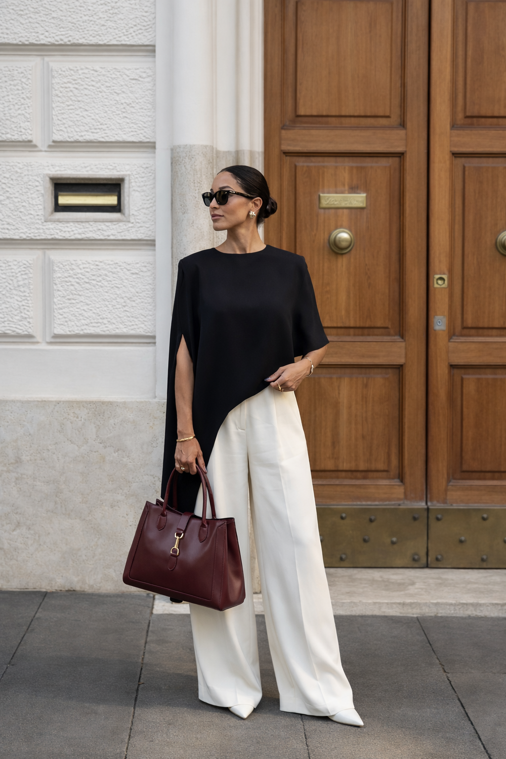 MALA EM PELE ITALIANA MANTOVA BURGUNDY | TUSCAN Mulher com roupa elegante e mala de couro castanha à frente de porta de madeira