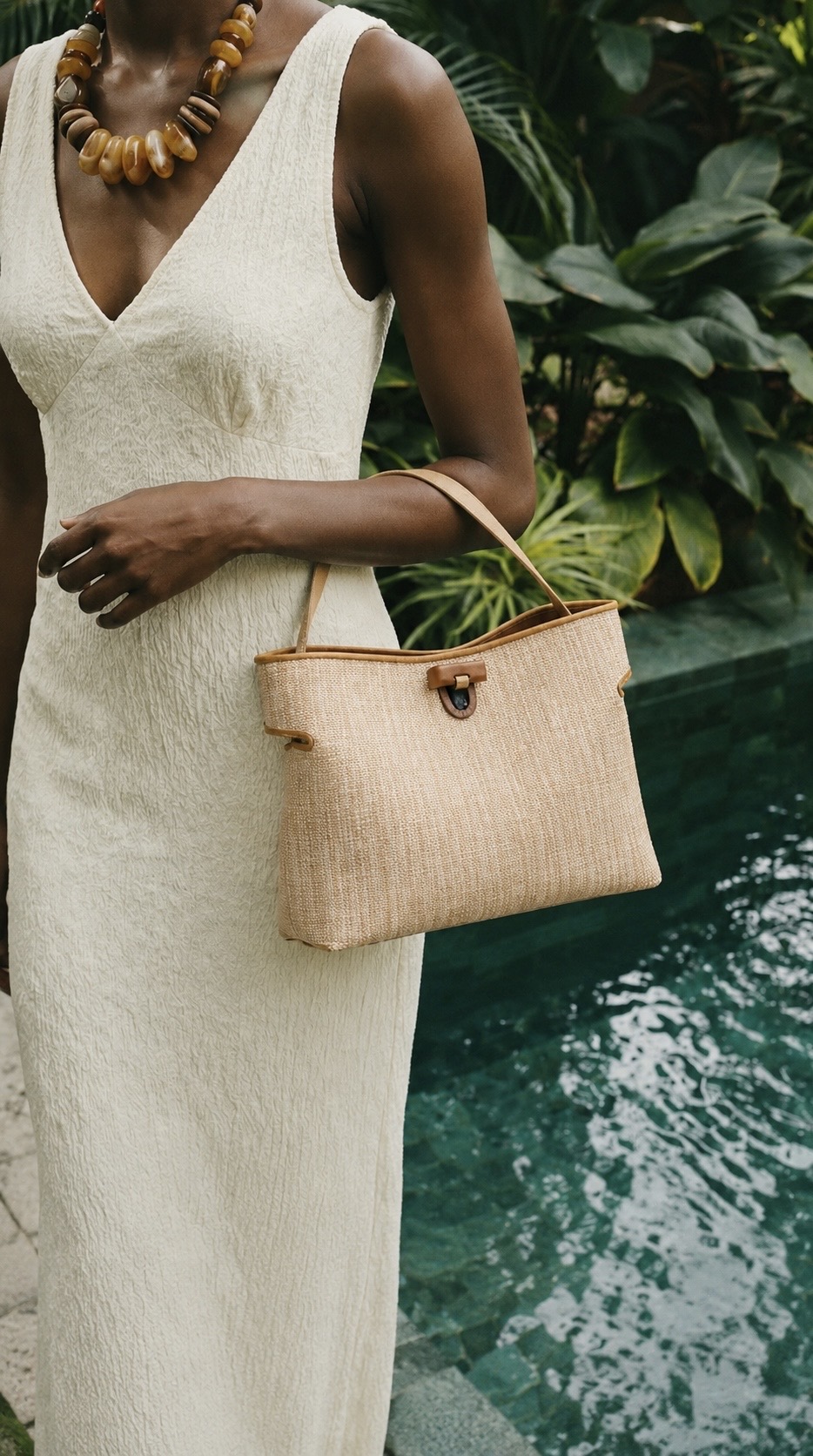 MALA EM PELE ITALIANA & RÁFIA | TUSCAN Mulher com vestido branco e mala bege perto de piscina com plantas ao fundo