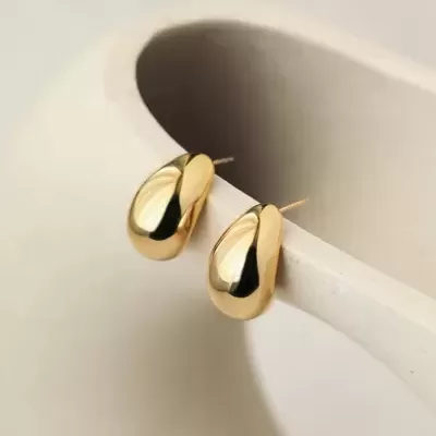 brincos dourados pequenos com acabamento brilhante sobre objeto cerâmico branco