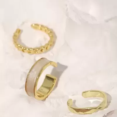 Três anéis dourados de estilos variados sobre fundo branco irregular