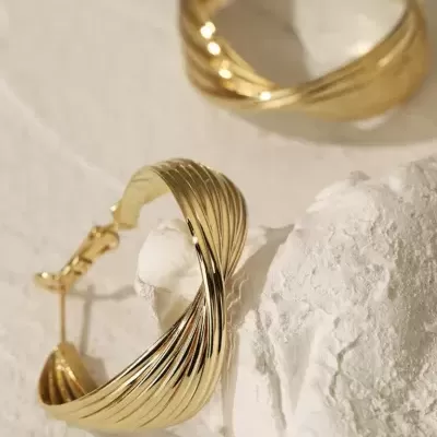 Brincos dourados entrelaçados sobre superfície branca texturizada