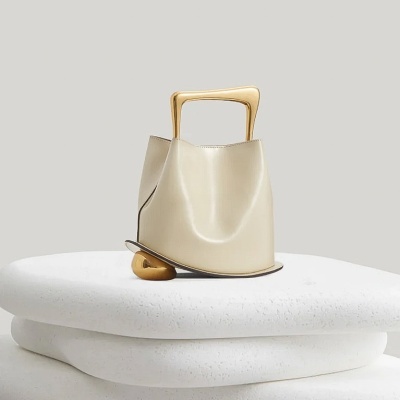 Mala de mão bege com alça dourada sobre bases brancas