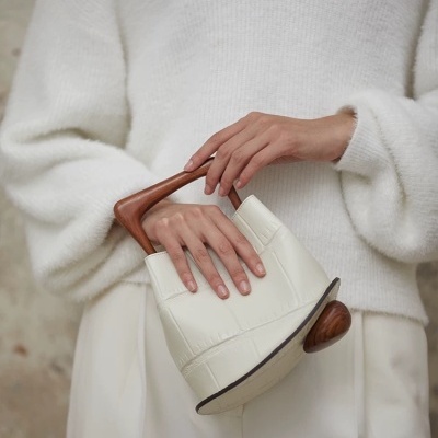 Sacola de mão branca acolchoada com alça de madeira nas mãos de pessoa com roupas brancas