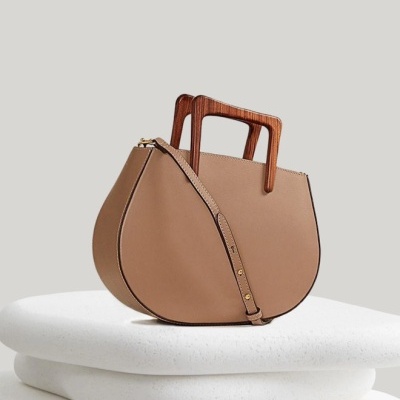 Mala de mão bege com alças de madeira sobre almofadas brancas