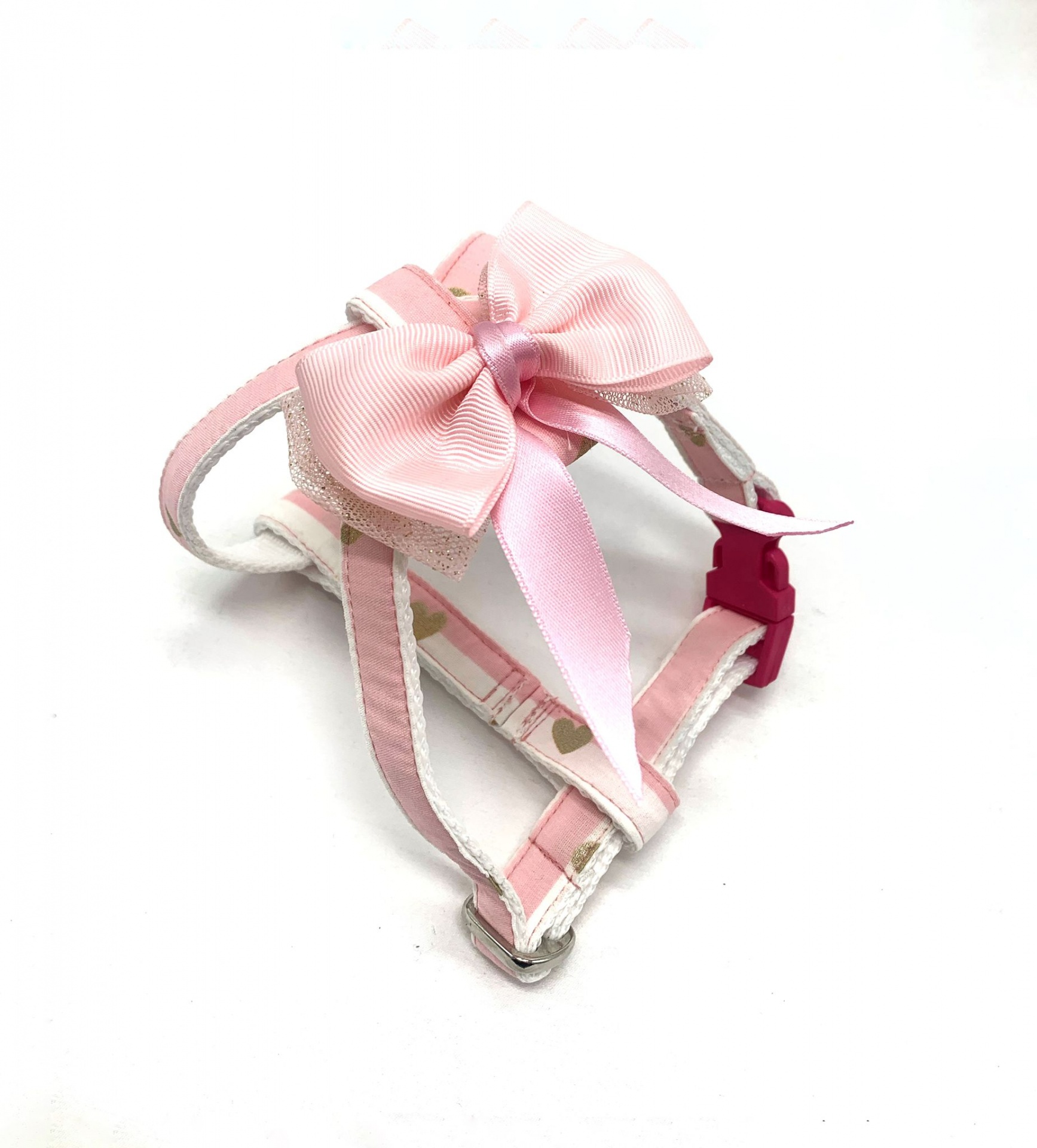 Peitoral para cão branco e rosa com padrão de corações e laço rosa.
