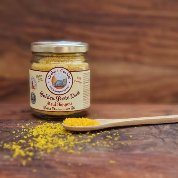 Frasco de vidro com pó amarelo Golden Paste Dust e colher de pau com pó na superfície de madeira.