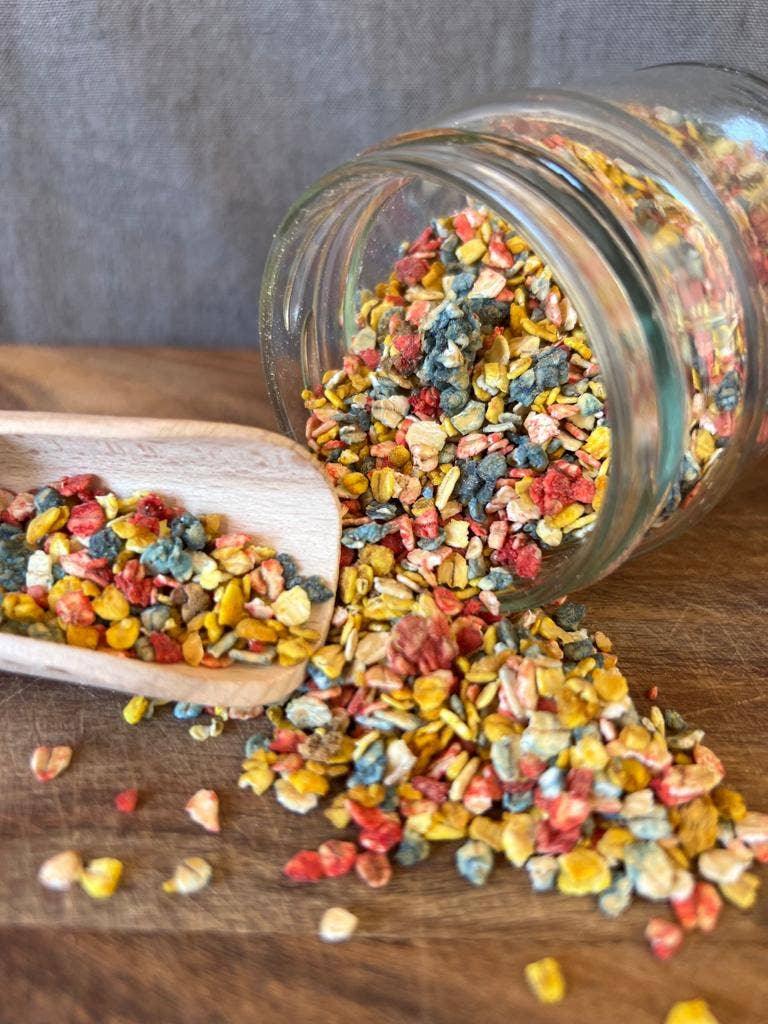 Frasco de vidro com partículas coloridas e colher de madeira numa tábua de madeira