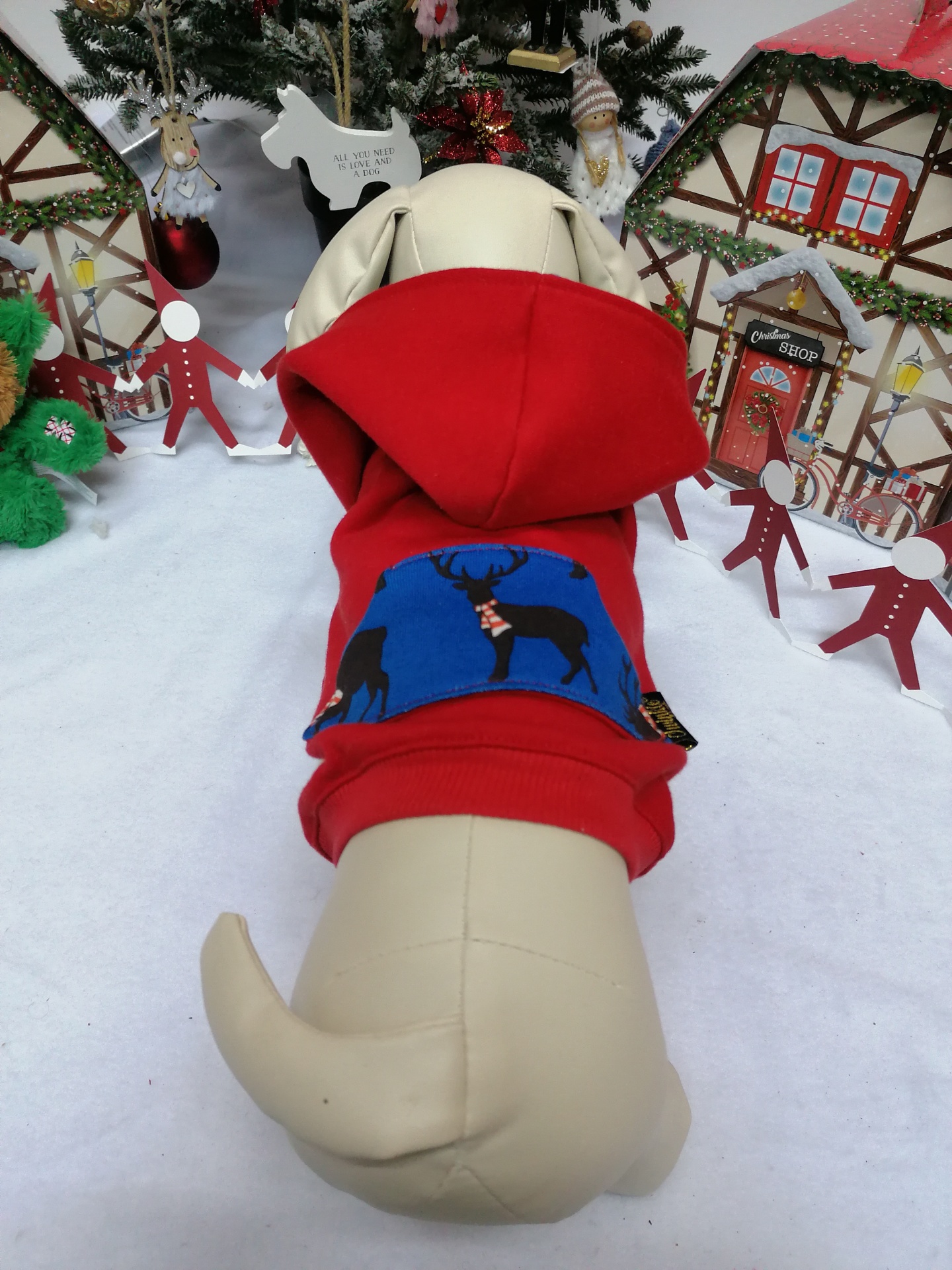 Casaco vermelho para cão com capuz e patch azul com veados, em decoração natalícia.