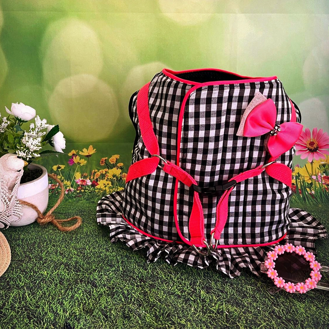 Colete para cão xadrez preto e branco com laço rosa e saia junto a colar rosa de flores em cenário com flores e relva