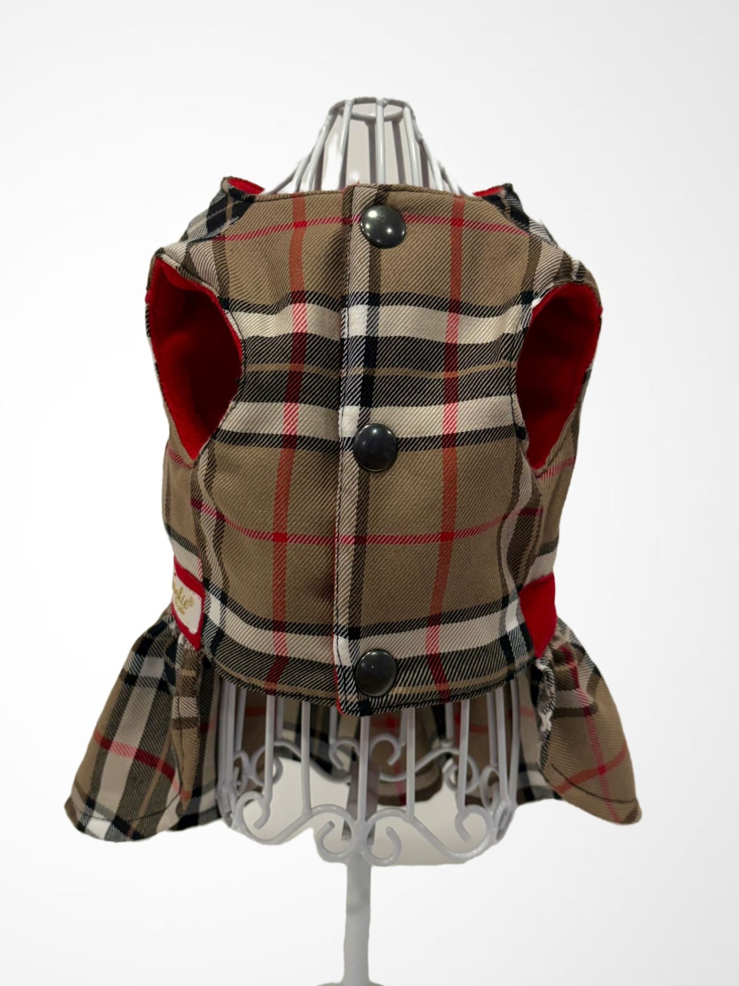 Casaco xadrez bege, preto, vermelho e branco com botões pretos e forro vermelho num suporte metálico branco